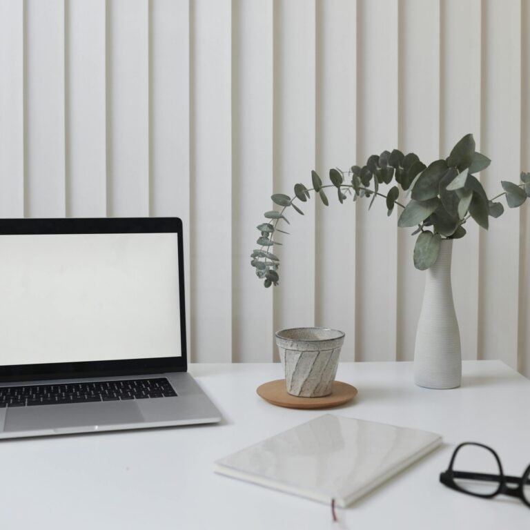 A clean and modern workspace featuring a laptop, vase with greenery, and notepad.