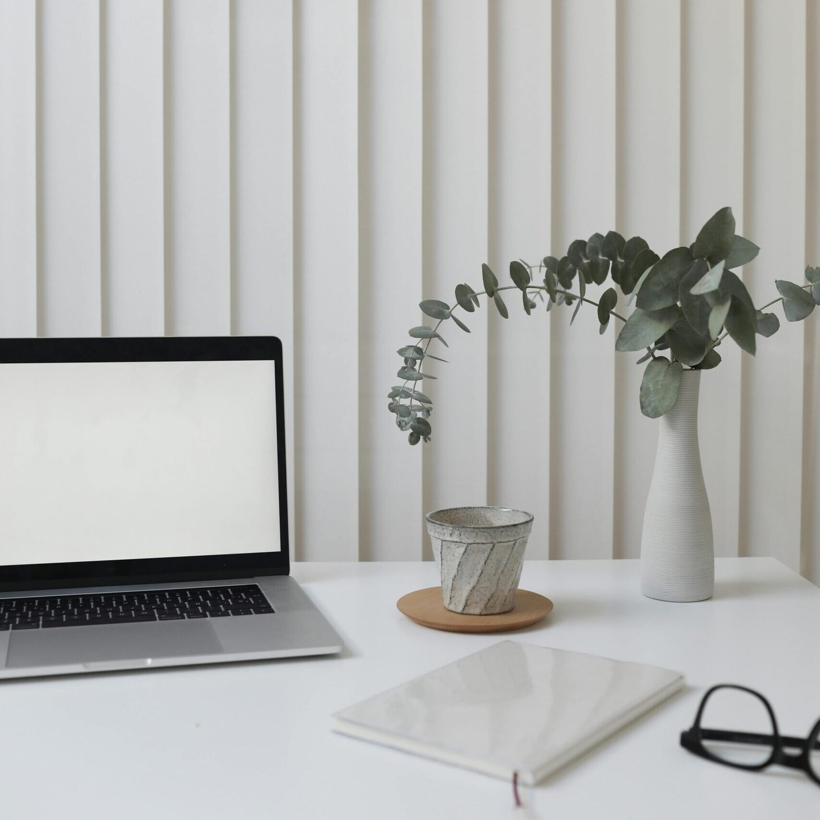 A clean and modern workspace featuring a laptop, vase with greenery, and notepad.